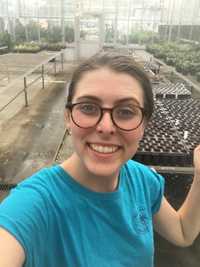 Hallie in a greenhouse while smiling at the camera.