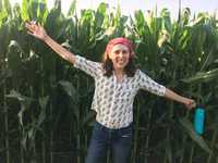 A woman smiling with her arms spread out wide while standing in front of a corn field